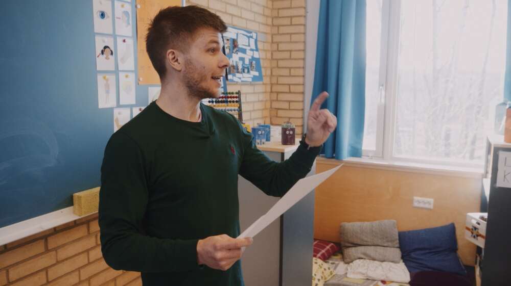Marius i klasserommet, foran tavle, snakker engasjert til elever utenfor bildet