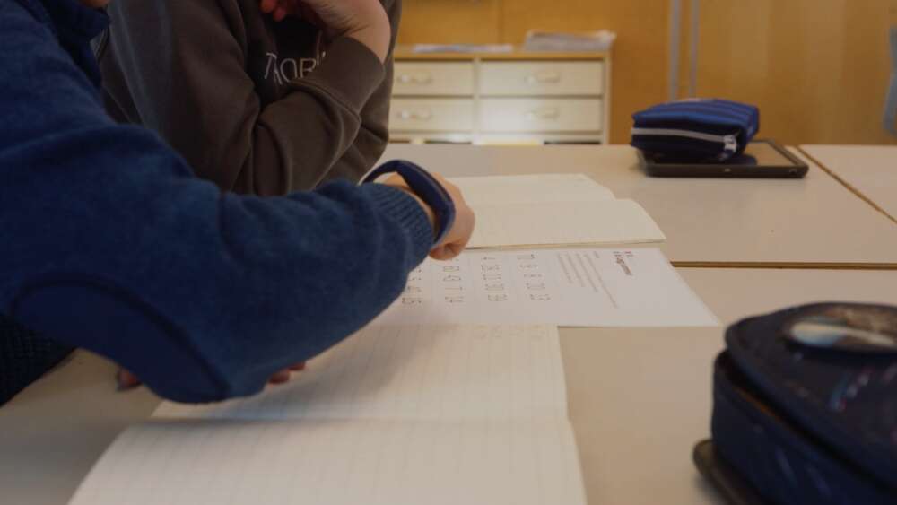 Utsnitt av to barn ved pulten. Ett av barnene peker på et ark med matematikk.