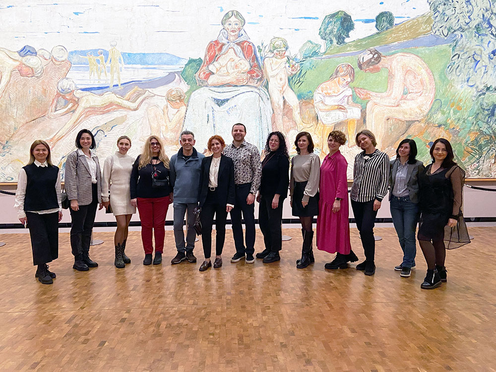 Gruppe med 13 mennesker på oppstilt foran et stort maleri